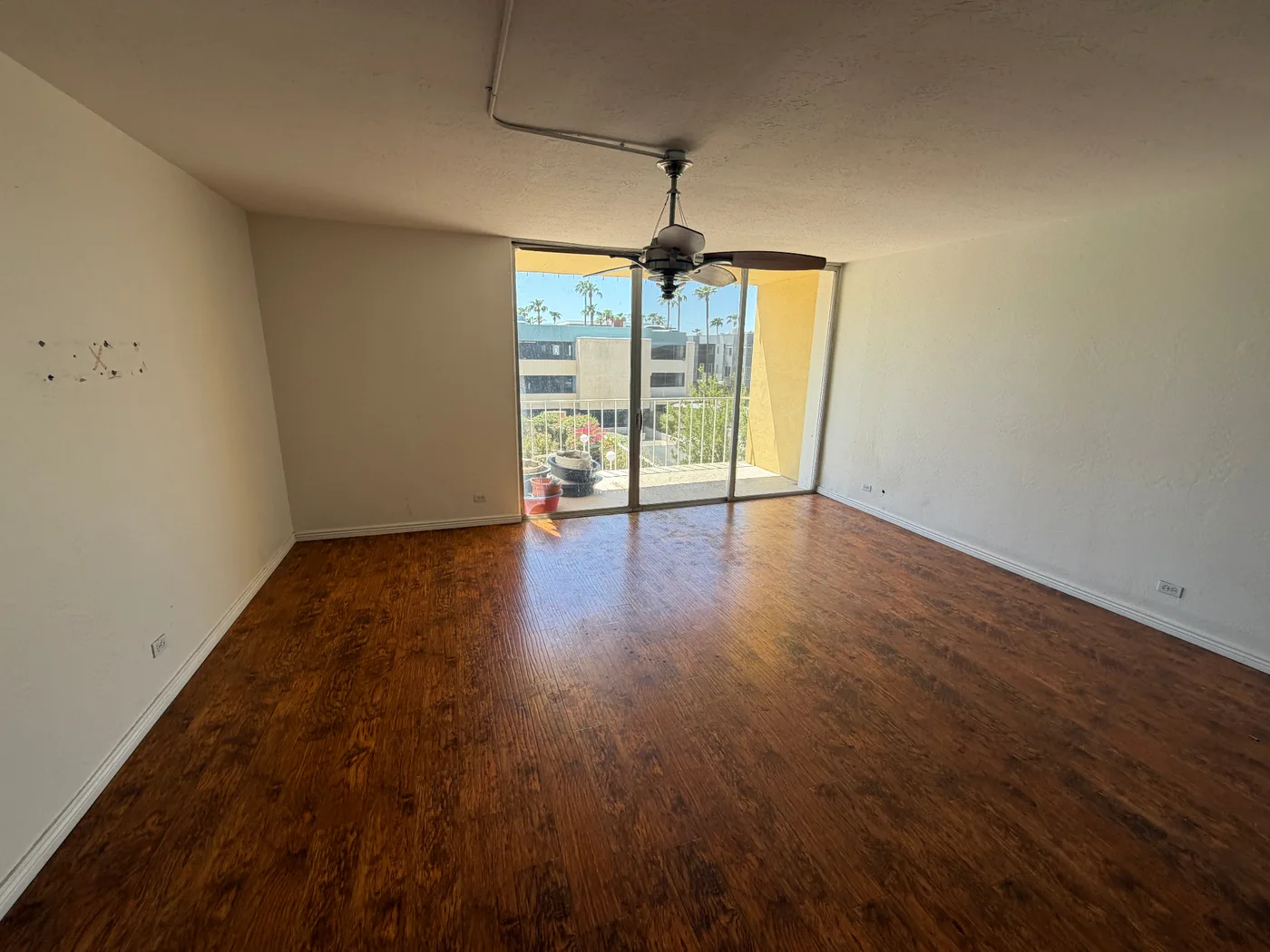 Condo living room before flooring removal, with existing flooring, ceiling fan and balcony doorway